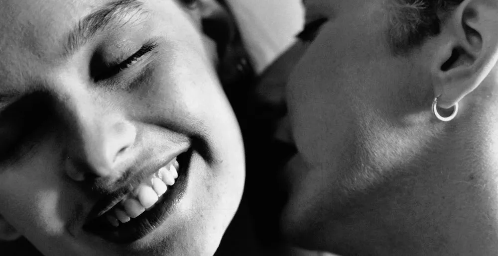 Close up of two faces, one kissing the other's neck. 