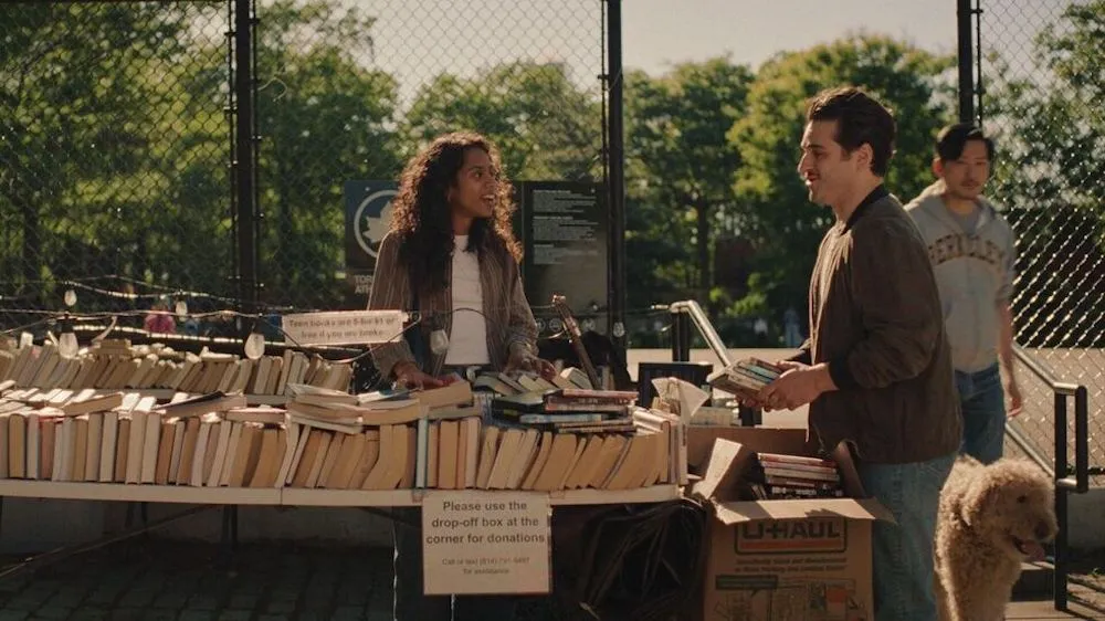 two people chat near a book cart outside