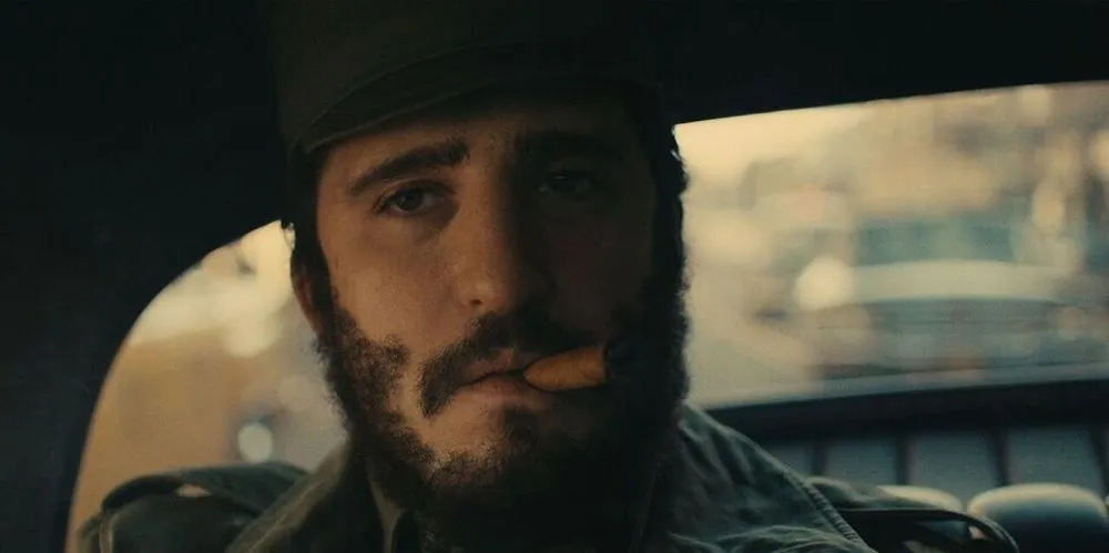 a man wearing a hat and smoking a cigar sits in the backseat of a car