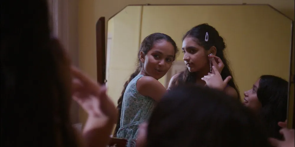 Three girls try on earrings in a mirror. 