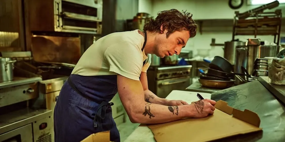 A man writes on a pizza box in a restaurant kitchen