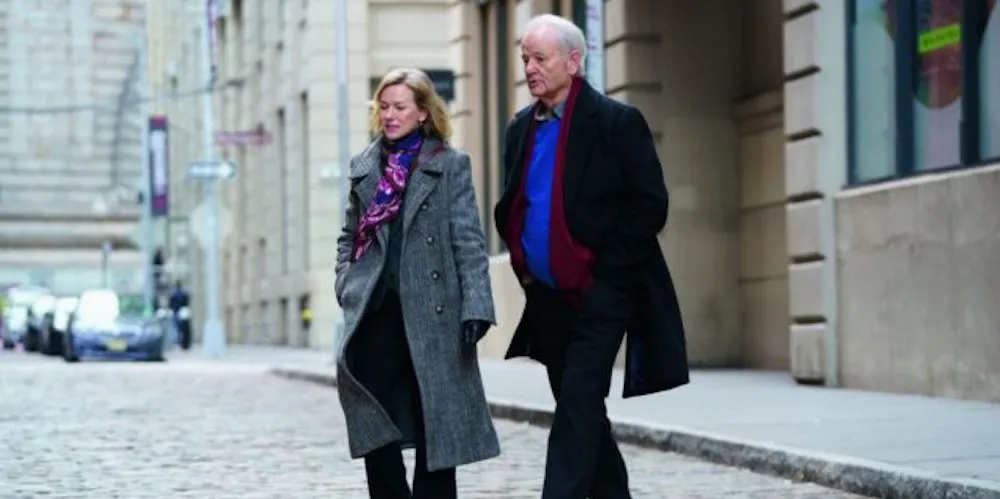 A man and woman in wool coats crossing a cobblestone street. 
