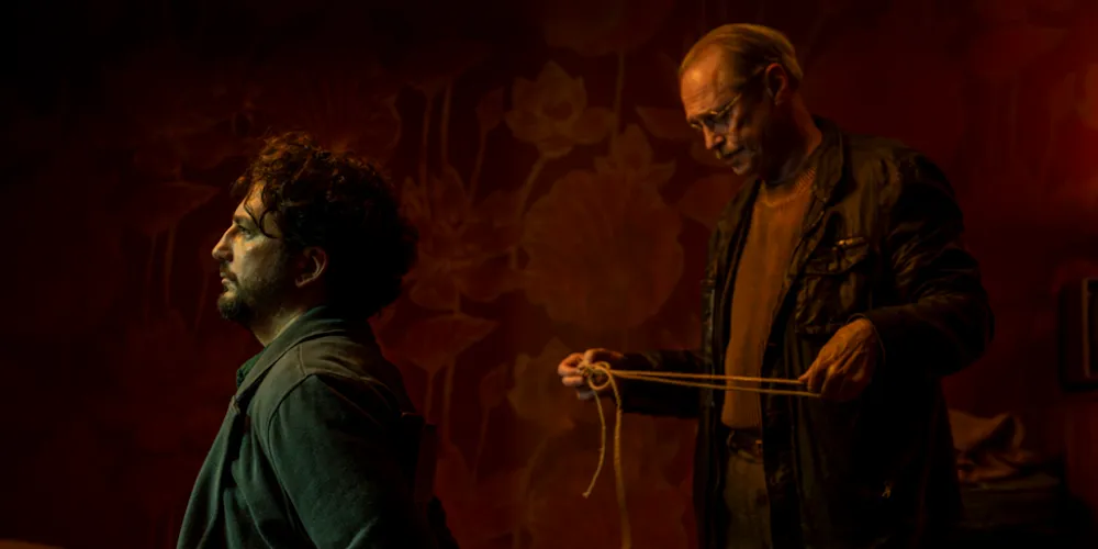 Two men, one kneeling, the other standing behind him with a rope. 