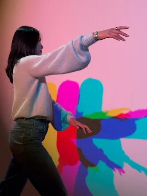 Woman posing in front of a projection of bold colors that become her shadow. 