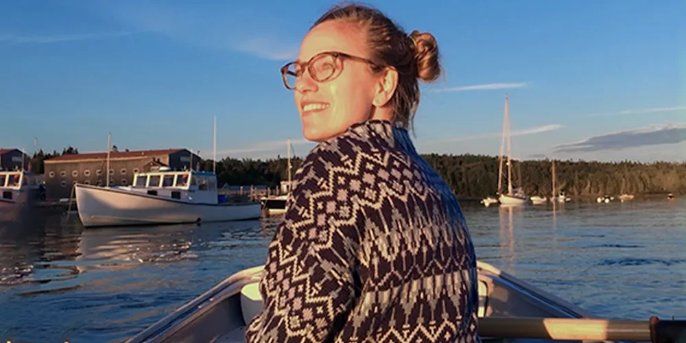 A woman on a small rowboat looks over her shoulder and smiles.