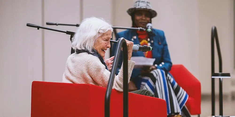 Two women sit on a stage, speaking into microphones.