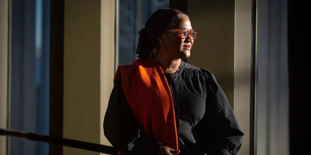 Lynn Nottage stands in a dimly lit room, looking out a window
