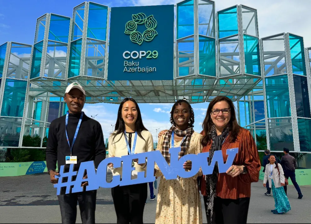 Four people stand in front of COP29 conference pavilion. 