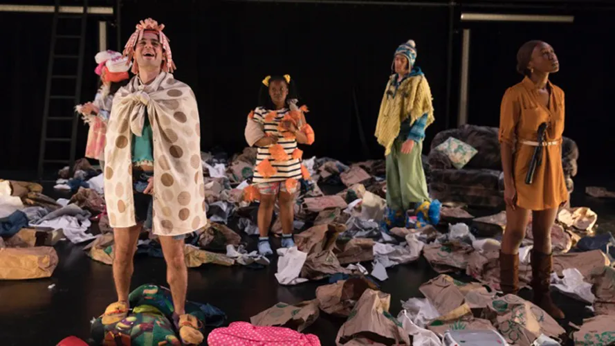 Four actors on stage surrounded by trash and clothes.