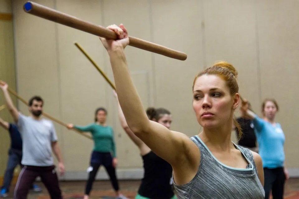 Jacqueline leading a class, all holding wooden dowels