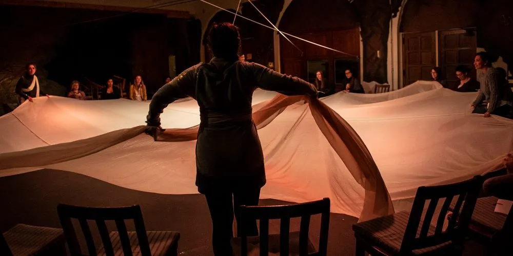 A group of people in a circle pulling up a blanket.