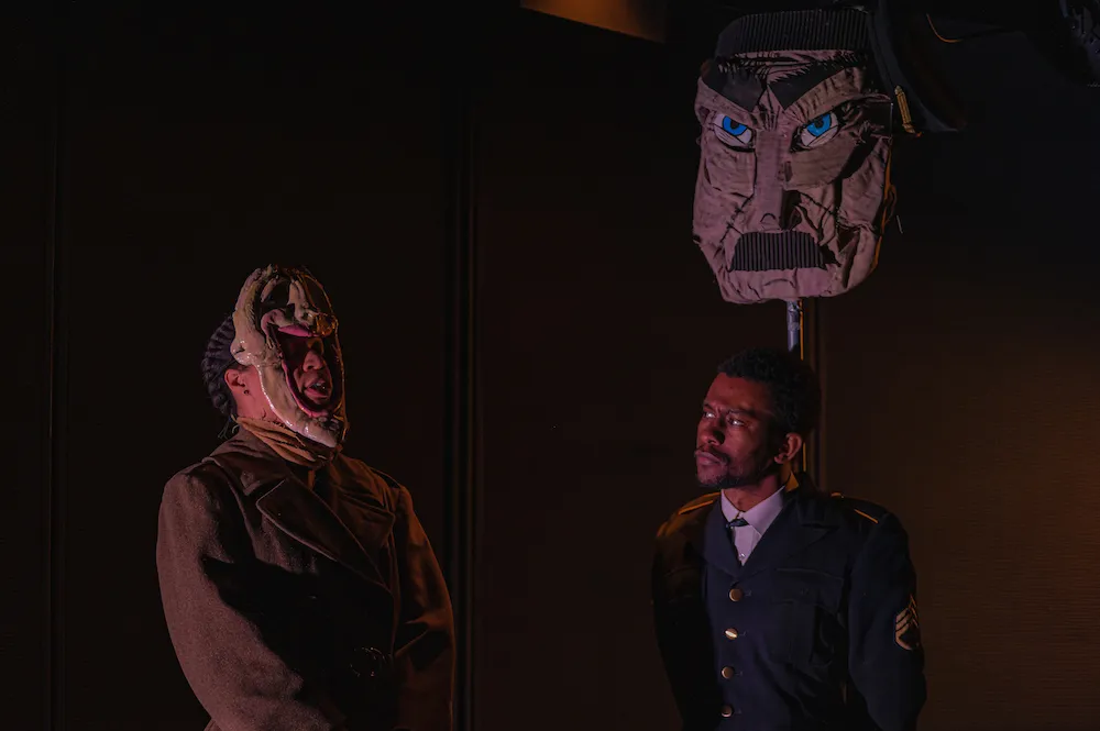 Two men stand in semi-darkness, wearing stylized masks. 