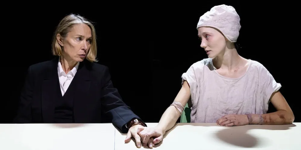 two actors on stage, sitting down holding hands