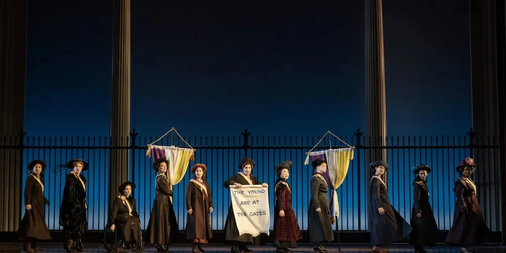 Women in historic costumes and banners on a stage.