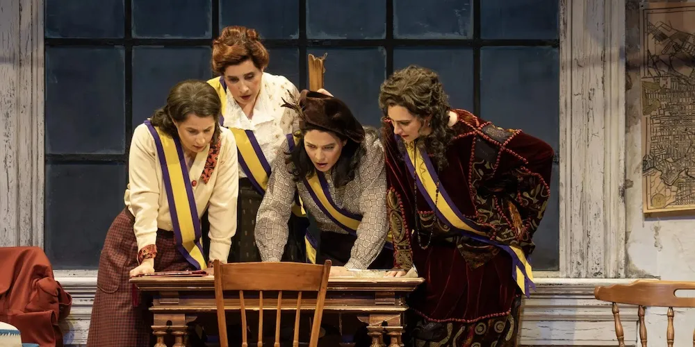 Four women looking at items on a desk. 