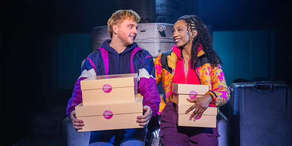 Two people in colorful tracksuits sit together holding boxes. 