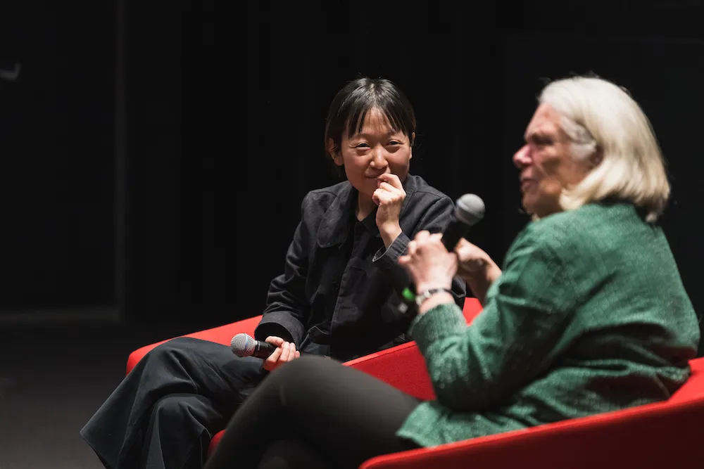 Anne Bogart holds speaks into microphone while Celine Song smiles. 
