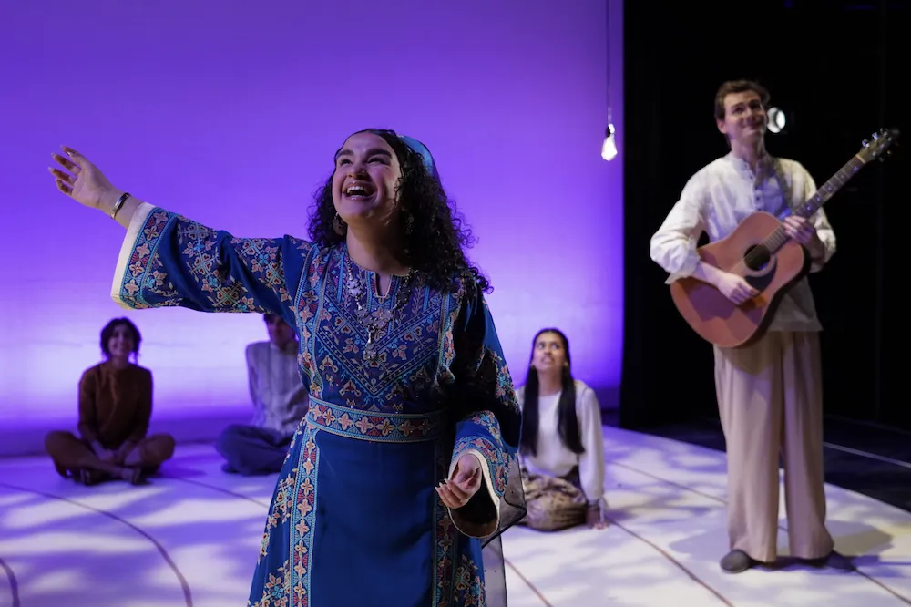 a group of actors perform on stage, one playing a guitar