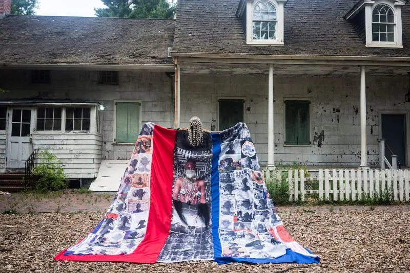 figure with cape posed in front of a house