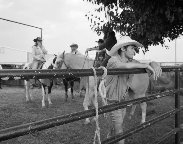 man in cowboy hat leaning on gate