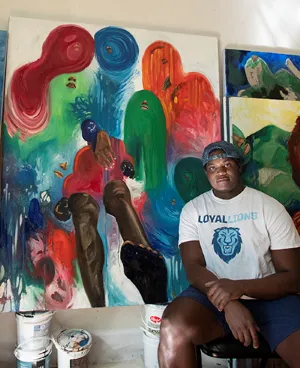 Khari Turner posing in front of his paintings.