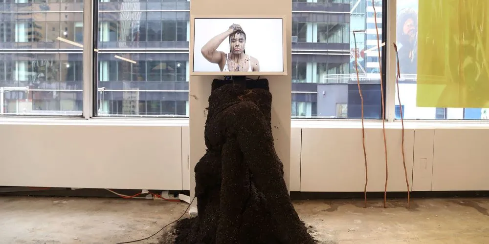 Art installation. A screen with the video of a woman and a sculpture under it.