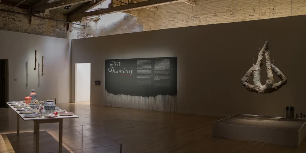Gallery space with low lighting and art hanging from the ceiling. 