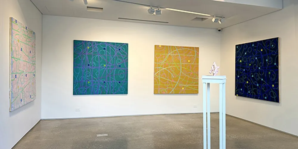 Four abstract paintings in a gallery. 
