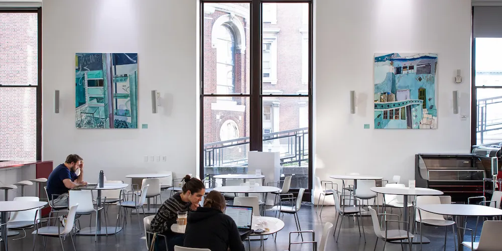 Two paintings hang in a cafe with a large bright window between them