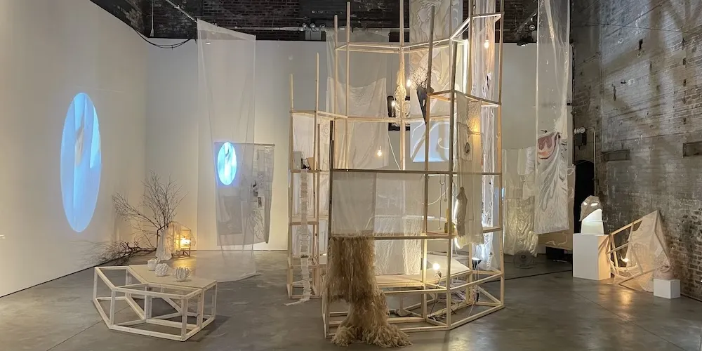 Art installation featuring a structure made out of light wood and transparent materials with projections on the materials and surrounding walls. 