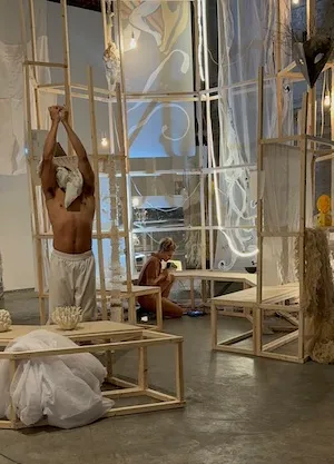 Two people interacting with an installation featuring a structure made out of light wood and transparent materials with projections on the materials and surrounding walls. 