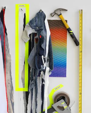 Materials such as a hammer, tape measure, jeans, and paper affixed to a wall. 