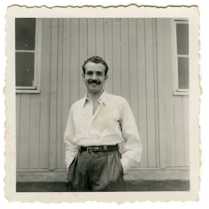 Old black and white photograph of man standing in front of building. 