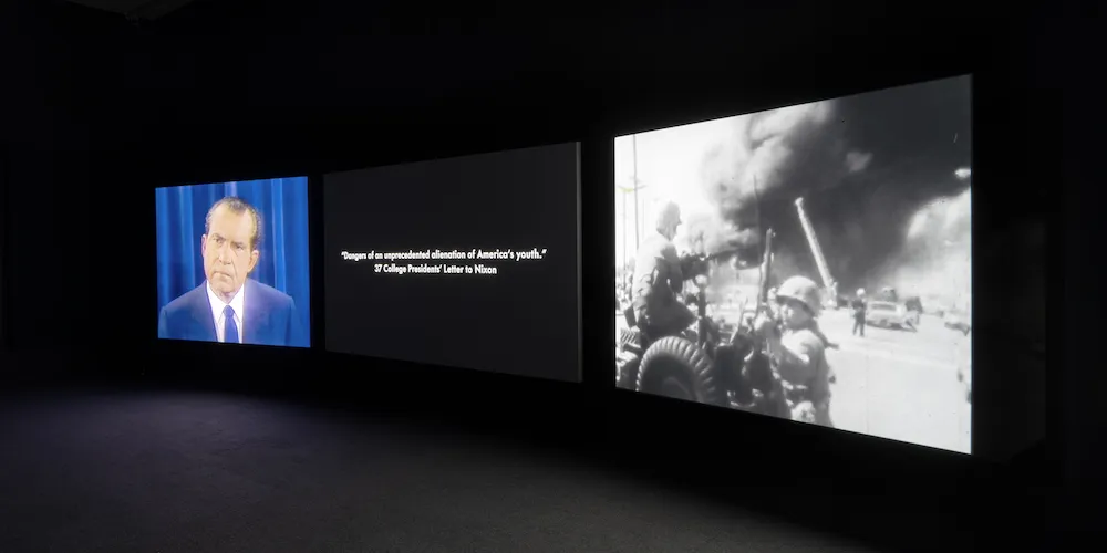 Three large screens displaying images against a black wall. 