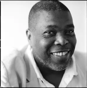 Black man in light collard shirt, smiling 