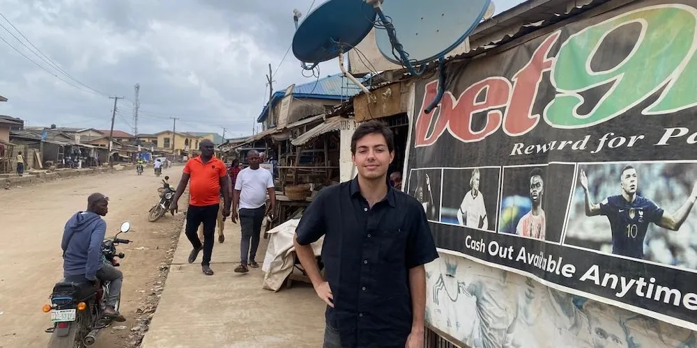 Young man stands on street next to "Bet9Ja" store sign. 