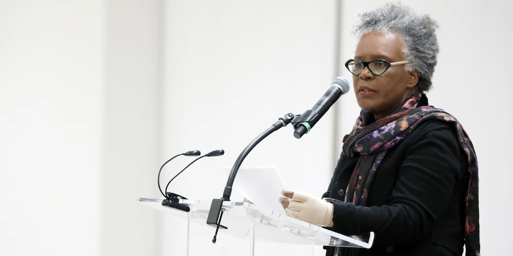 A woman stands at a podium, speaking into a microphone. 