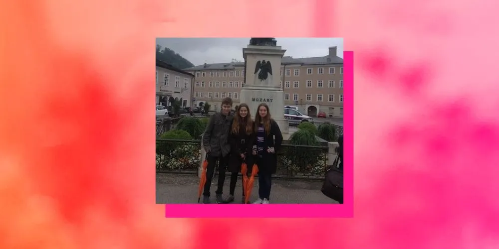 Three people in front of green bushes and a building