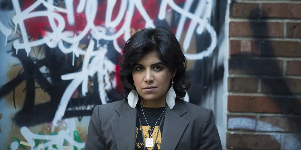 Current student Nada Faris in front of a brick wall with graffiti letters.