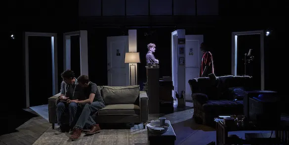 Actors sit on couches and stand on a dark stage filled with several open doorways