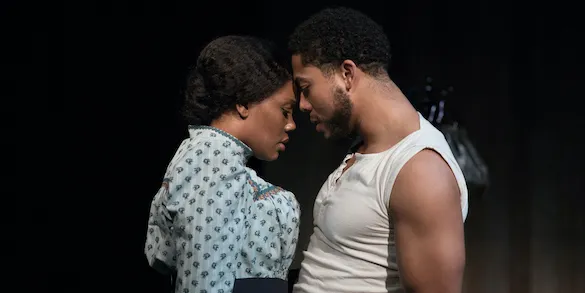 A man and woman stand close on stage, their foreheads touching