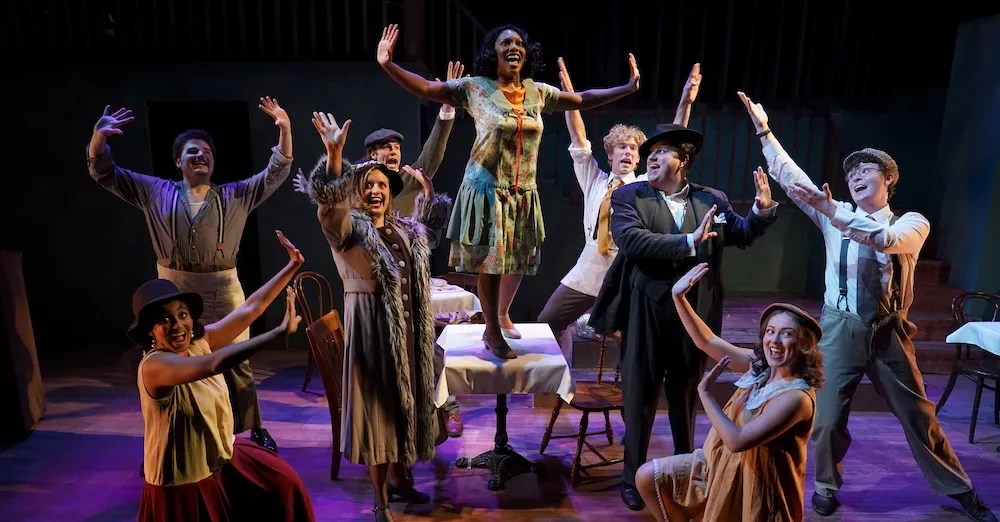 a group of actors sing on stage with their hands in the air