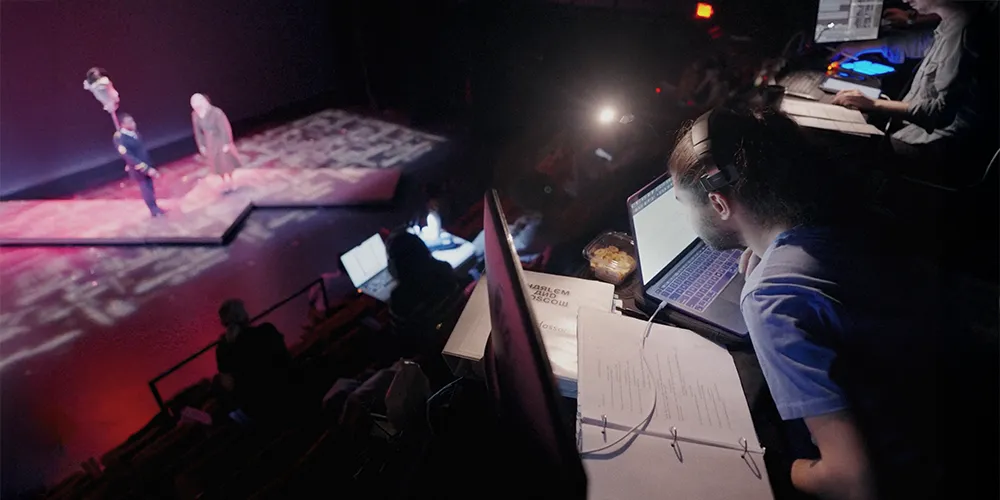 a student sits at a desk with a laptop watching a performance on the stage below