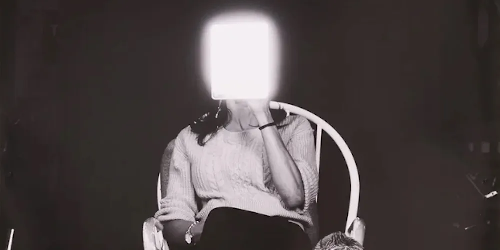 a woman sits in a chair, holding a mirror in front of her face