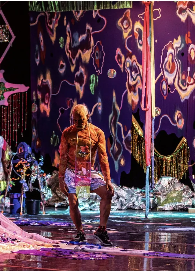Man poses on a colorful stage with a psychedelic backdrop. 