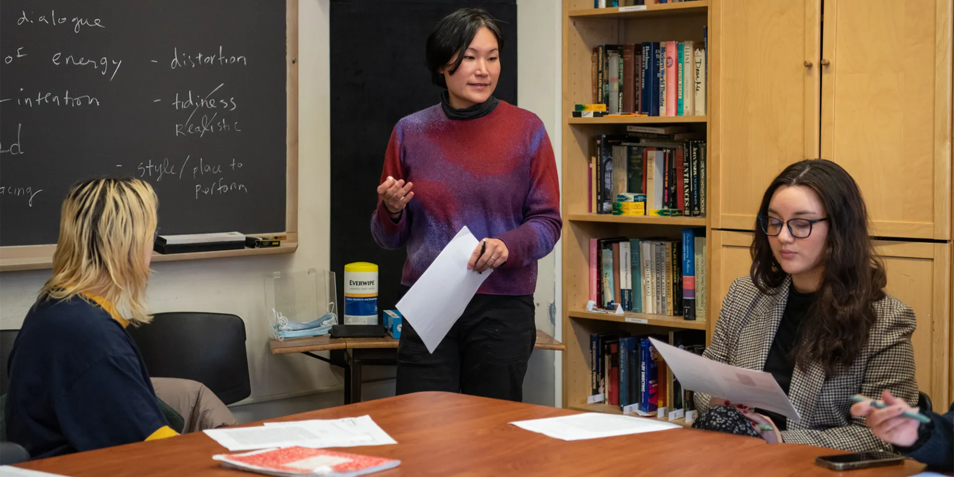 A professor stands in front of a chalkboard, teaching a group of students.