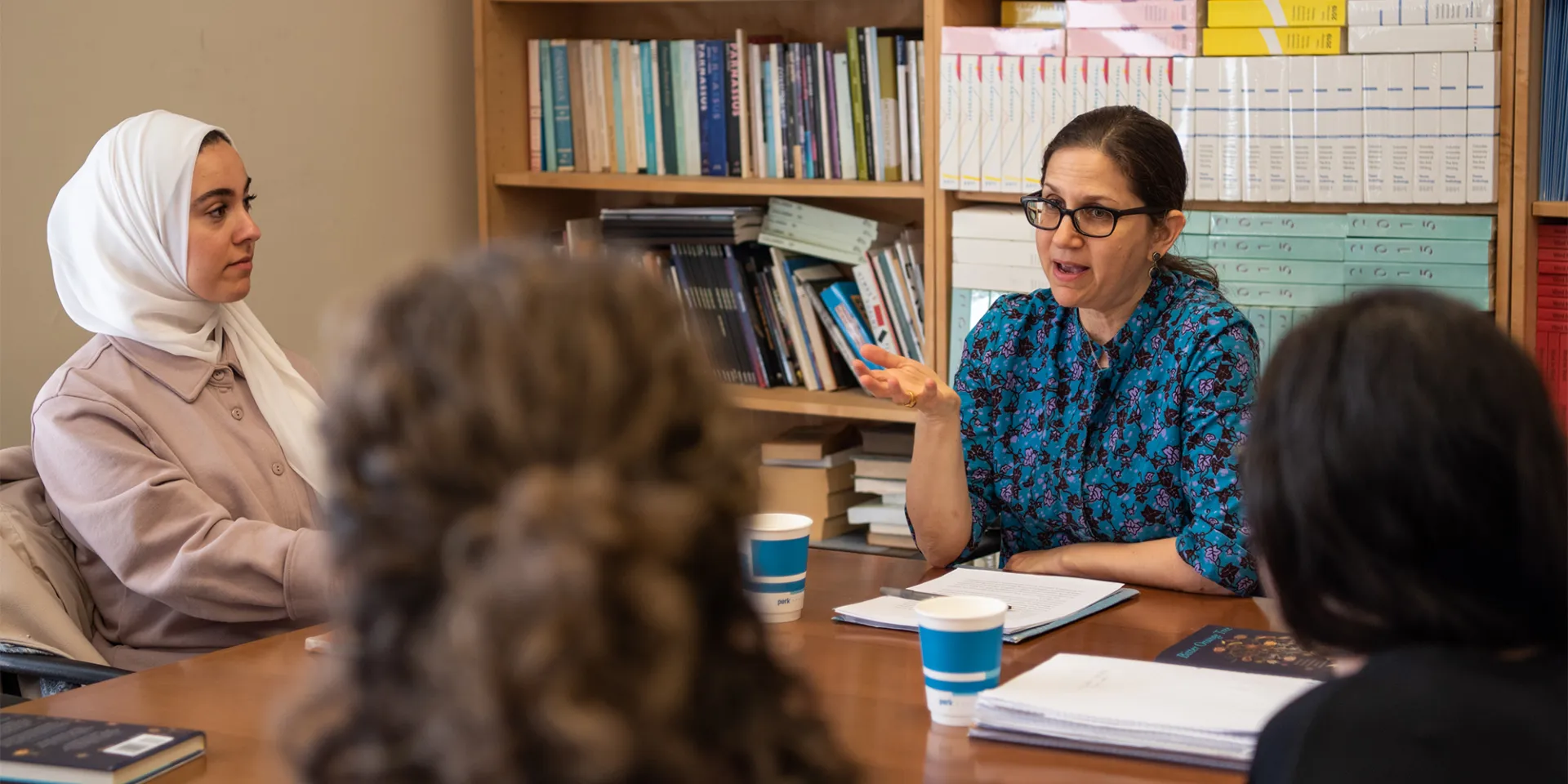 A professor sits at a table with a group of students
