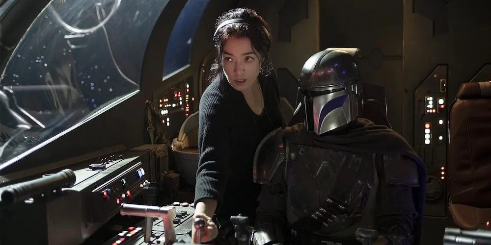 An Asian American woman directing a man in a costume