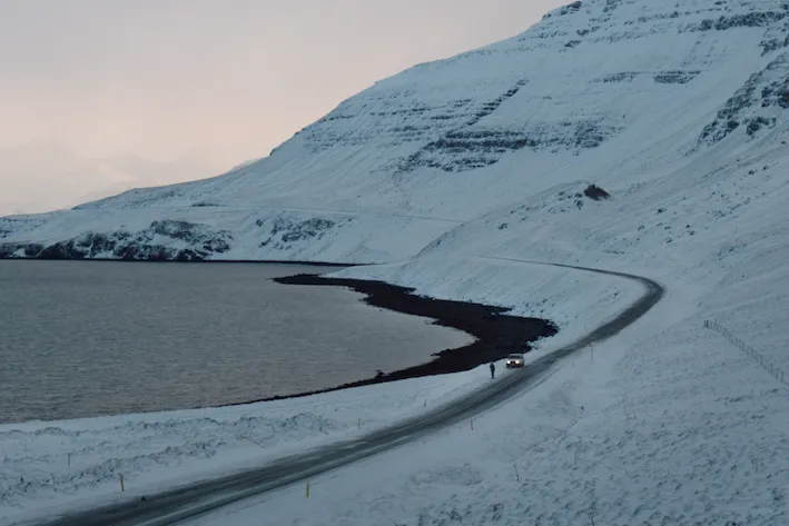 Snowy mountain scene with a road and person standing in the middle of it 