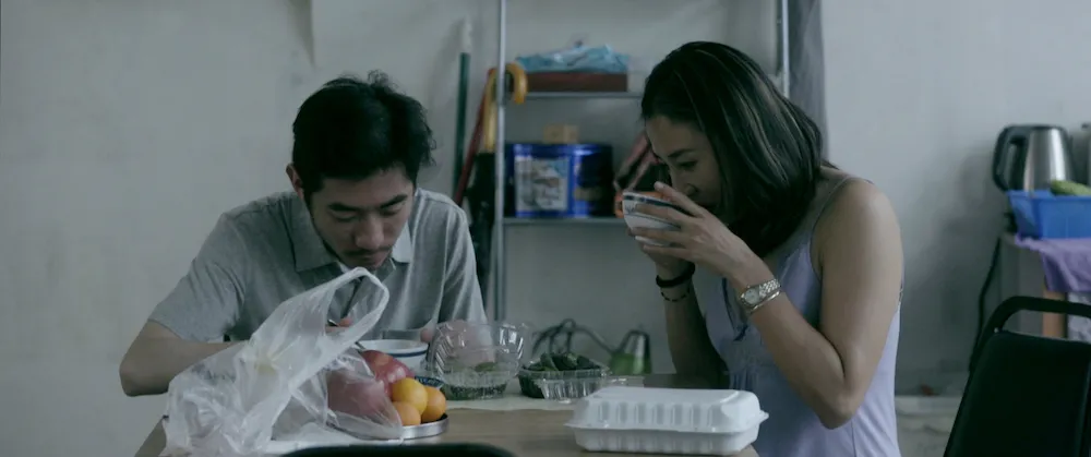 Two Asian people—a man and a woman—sitting at a table eating soup.